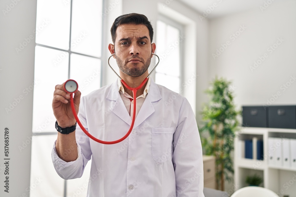 Young hispanic doctor man with beard holding stethoscope auscultating depressed and worry for distress, crying angry and afraid. sad expression.