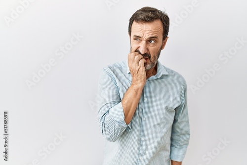 Middle age hispanic man with beard standing over isolated background looking stressed and nervous with hands on mouth biting nails. anxiety problem.