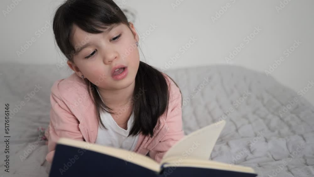 Little girl laying on the bed reading book. Study at home, Homeschooling concept. cozy leisure time. Kid watch to the notebook with open mouth. Little girl laying on the bed reading book. Study at home, Homeschooling concept. cozy leisure time. Kid watch to the notebook with open mouth.