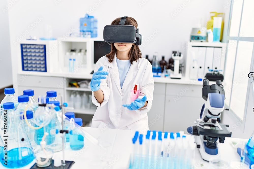 Fototapeta premium Young hispanic girl wearing virtual reality glasses at laboratory