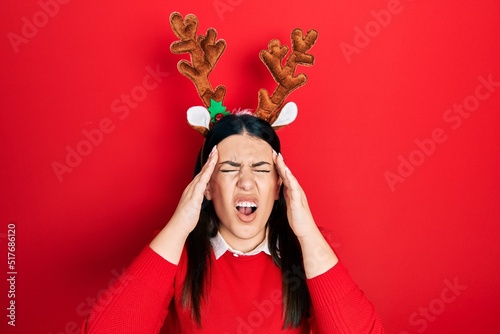 Print op canvas Young hispanic woman wearing cute christmas reindeer horns suffering from headache desperate and stressed because pain and migraine