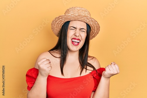 Young hispanic woman wearing summer hat excited for success with arms raised and eyes closed celebrating victory smiling. winner concept.