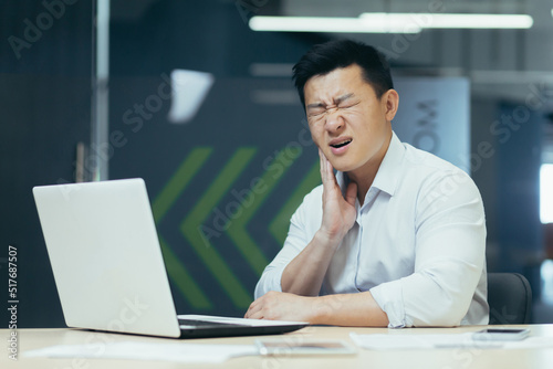 Asian man working in modern office, businessman having severe toothache, sick employee at work.