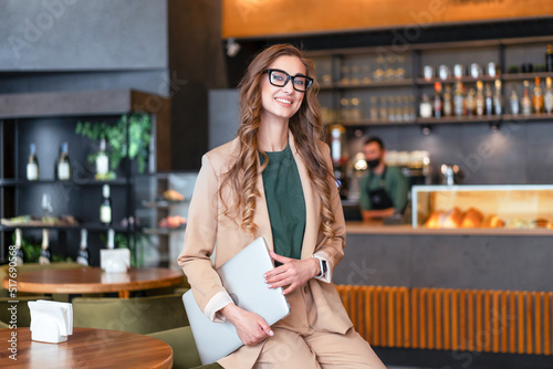 Business Woman Restaurant Owner With Laptop In Hands Dressed Elegant Pantsuit Standing In Restaurant With Bar Counter Background