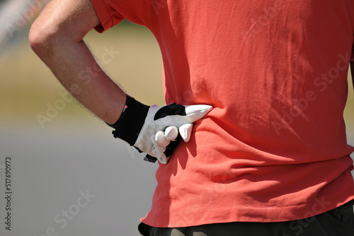A hobby goalkeeper in an orange shirt supports his left arm on the side of his body.