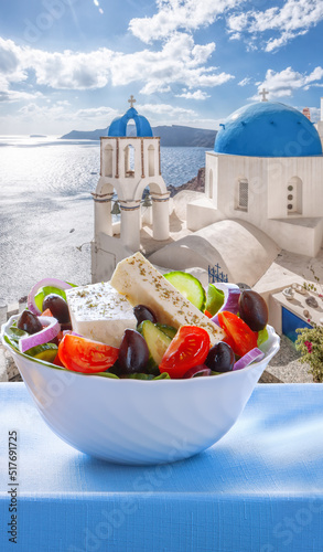 Greek salad against famous church in Oia village on Santorini island in Greece
