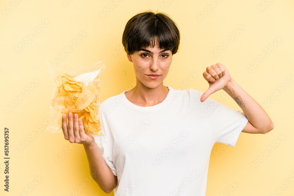 Young caucasian man holding crisps isolated on yellow background showing a dislike gesture, thumbs down. Disagreement concept. Young caucasian man holding crisps isolated on yellow background showing a dislike gesture, thumbs down. Disagreement concept.