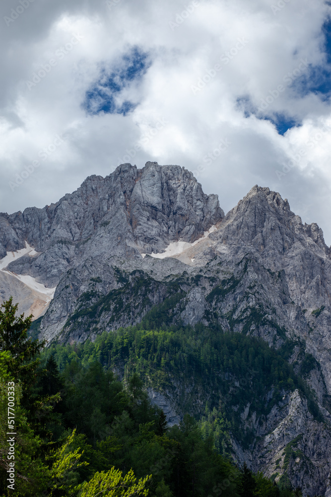 The peaks of Triglav National Park in Slovenia. The peaks are in the sun. The sky is overcast but shows blue skies.