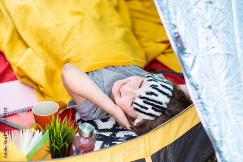 happy child in a sleep mask lies in a tourist tent in the forest