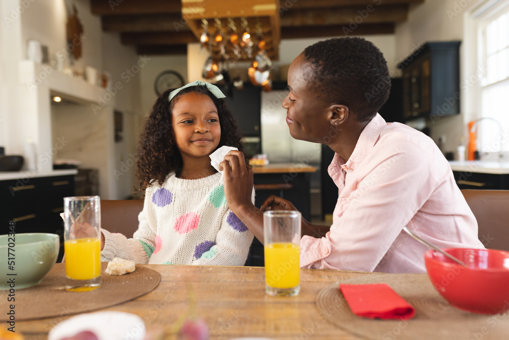 Image of happy african american girl eating breakfast with mother