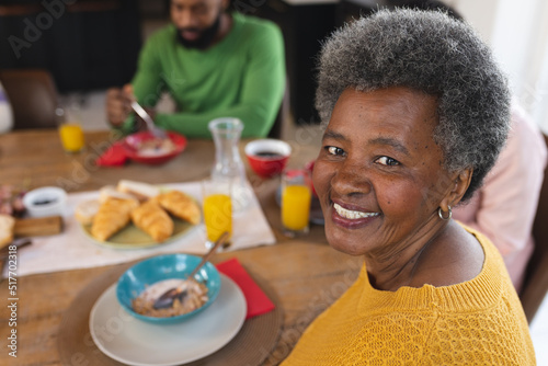 Image of happy african american senior woman eating breakfast with family