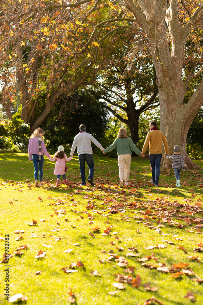 Fototapeta premium Vertical image of back view of multi generation caucasian family spending time in autumn garden