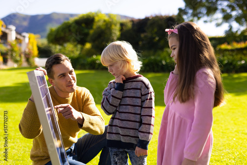 Image of caucasian father showing solar panel to children