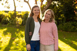 Image of happy caucasian mother and adult daughter posing at camera in autumn garden