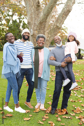 Vertical image of happy multi generation african american family posing at camera outdoors in autumn