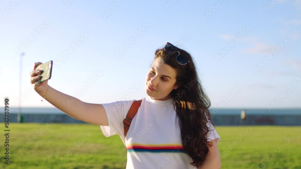 Young student taking selfie in the park on her phone. Happy female tourist shows peace sign for a photo on a summer day. Cool, fresh and trendy millennial makes a silly face for selfie. Young student taking selfie in the park on her phone. Happy female tourist shows peace sign for a photo on a summer day. Cool, fresh and trendy millennial makes a silly face for selfie.