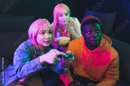 Indoor shot of a group of interracial millenial people playing video games, sitting on a dark sofa. Asian female teenager winnig a competition and cheering. High quality photo photo