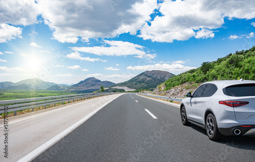 A white car drives along a beautiful road on a sunny summer day.