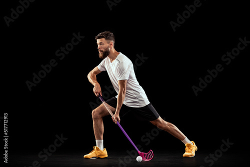 Studio shot of young man wearing sports uniform and sneakers playing floorball isolated on dark background. Sport, action and motion, movement, competition