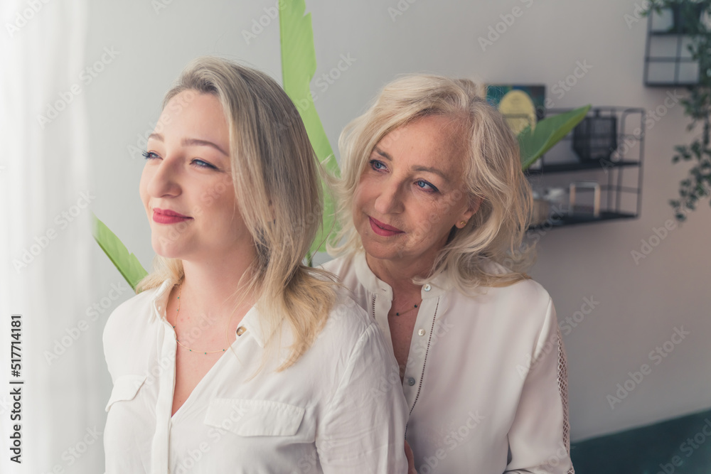 Two attractive elegant women i- mother and daughters with blonde hair standing close to each other. One woman supporting the other one, kissing her in her cheek. High quality 4k footage. High quality Two attractive elegant women i- mother and daughters with blonde hair standing close to each other. One woman supporting the other one, kissing her in her cheek. High quality 4k footage. High quality