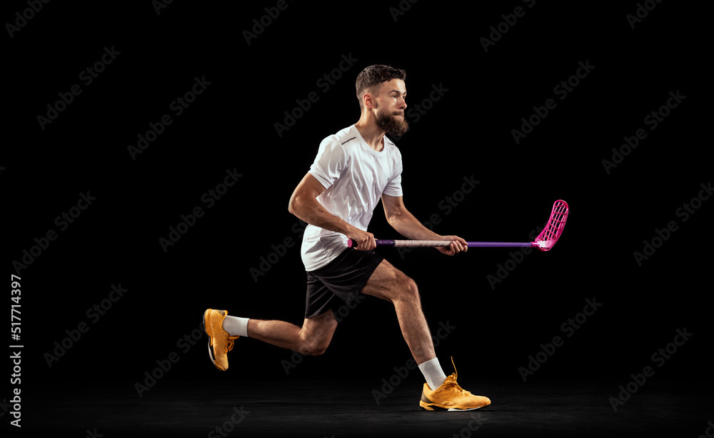 Studio shot of young man wearing sports uniform and sneakers playing floorball isolated on dark background. Sport, action and motion, movement, competition