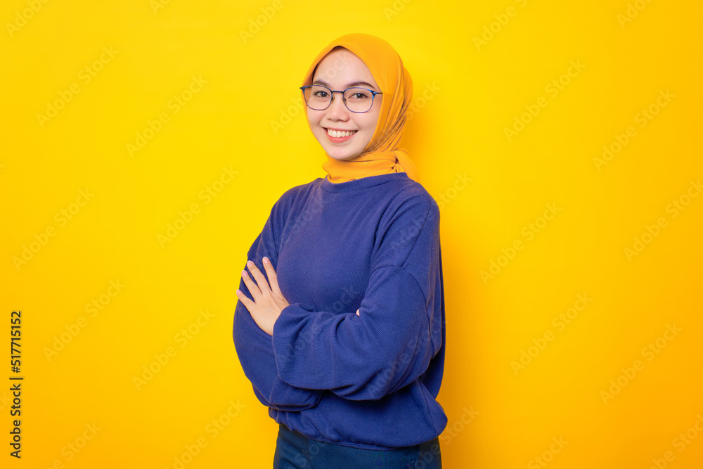 Fototapeta premium Smiling young Asian Muslim woman dressed in casual sweater crossed arms and looking confident isolated over yellow background