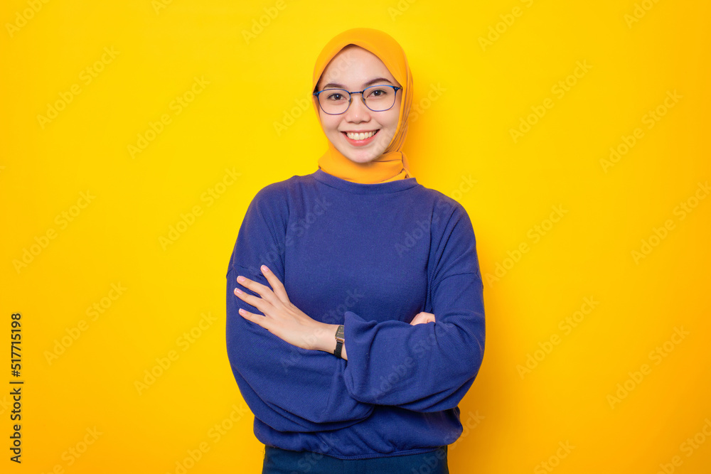 Smiling young Asian Muslim woman dressed in casual sweater crossed arms and looking confident isolated over yellow background Smiling young Asian Muslim woman dressed in casual sweater crossed arms and looking confident isolated over yellow background