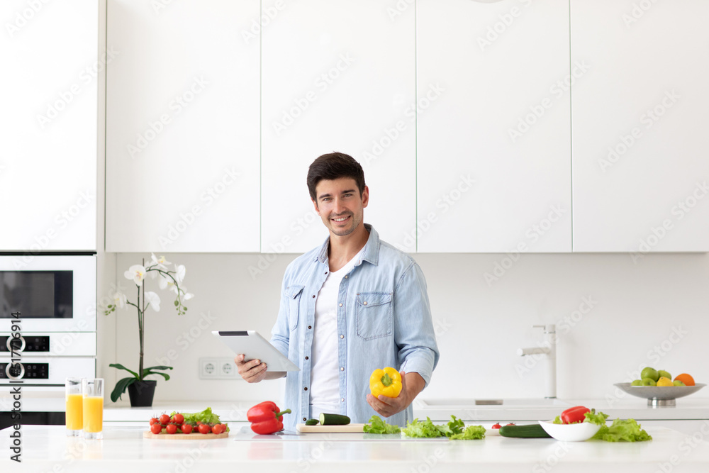 Young smiling man while preparing vegetable salad in the kitchen
