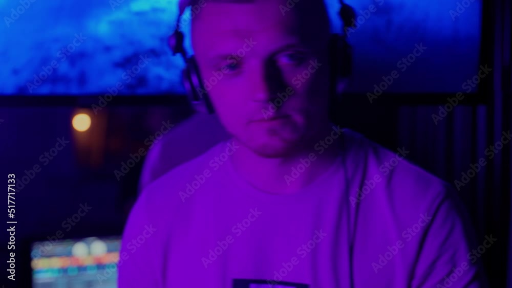 Man DJ working in club in neon lights indoors. Caucasian male person using headphones to mix music and change volume sound. Purple light in nightclub room. Jockey on disco party. Nightlife in city Man DJ working in club in neon lights indoors. Caucasian male person using headphones to mix music and change volume sound. Purple light in nightclub room. Jockey on disco party. Nightlife in city