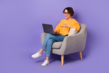 Portrait of attractive cheerful girl sitting using netbook calling on web communicating isolated over violet lilac color background