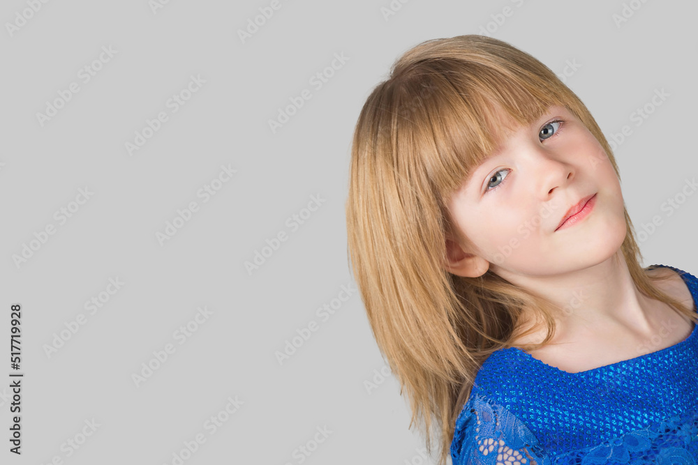 Portrait of a girl of six years old dressed in a blue elegant dress, in the studio on a gray background. The child emotionally poses for a camera. Portrait of a girl of six years old dressed in a blue elegant dress, in the studio on a gray background. The child emotionally poses for a camera.