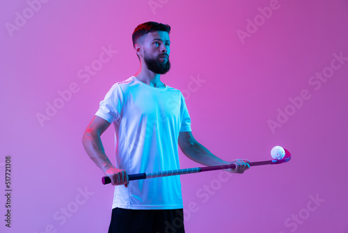 One sportive man, floorball player with floorball stick training isolated on lilac color background in neon. Sport, action and motion, movement, healthy lifestyle photo