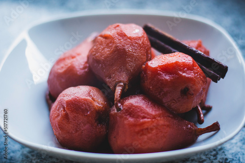 Closeup of stewed pears poached in red wine and served on a white bowl.