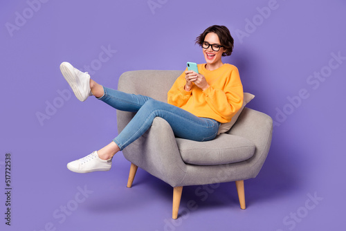 Portrait of attractive cheerful girl sitting using device communicating having fun rest isolated over violet lilac color background photo