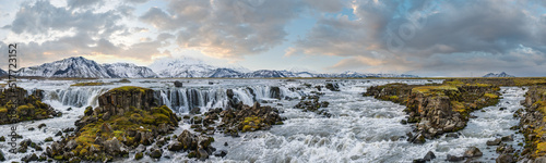Season changing in southern Highlands of Iceland. Picturesque waterfal Tungnaarfellsfoss panoramic autumn view. Landmannalaugar mountains under snow cover in far.