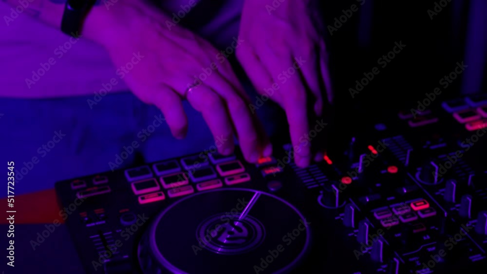 DJ using console in club in neon lights close up. Male person touching twist buttons on control device by hands and change the music tones. Jockey on disco party in nightclub. Nightlife concept