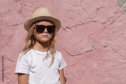 A preteen girl poses for the camera against a pink wall.