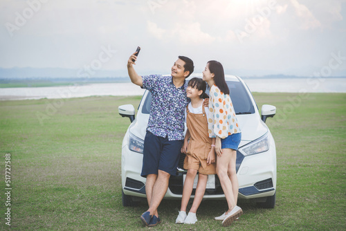 Happy Family with father mother and daughter selfie and looking smartphone and having fun on a tropical beach and a car on the sider. Family vacation holiday and travel concept. photo