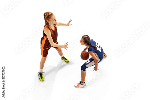 Play defense. Two basketball players, young girls, teen training with basketball ball isolated on white background. Concept of sport, team, enegry, competition, skills