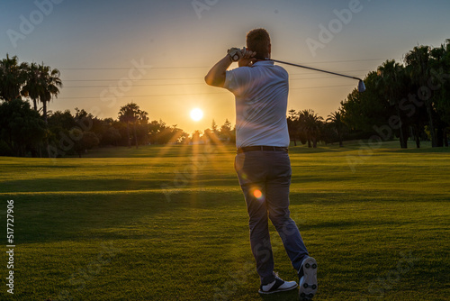 Good strike, professional golfer looking trajectory of the ball, golfer hitting golf ball standing on course at sunny evening