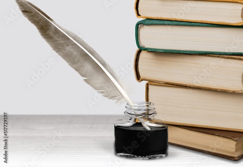 Feather quill pen with a vintage ink well and a stack of old books, the concept of writing