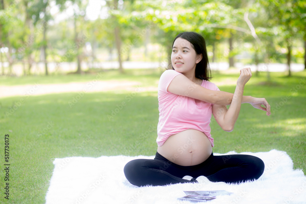 Happiness young asian woman pregnant sitting doing sport exercise with stretch hands muscle for health care at park, mother practicing yoga for leisure in the garden, activity for pregnancy concept. Happiness young asian woman pregnant sitting doing sport exercise with stretch hands muscle for health care at park, mother practicing yoga for leisure in the garden, activity for pregnancy concept.