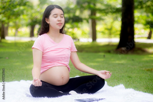 Happiness young asian woman pregnant sitting doing yoga with meditation lotus for relaxation in the park, mother practicing workout for health in the garden, exercise or sport for pregnancy concept. © N_studio