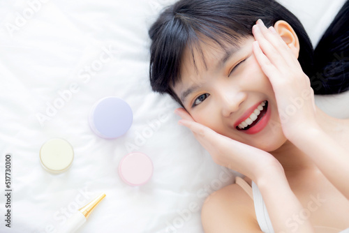 Beautiful of young asian woman smiling and lying on bed with cosmetic at bedroom, beauty of girl with hygiene and healthy, cream and lotion and skin care, top view, skincare and lifestyles concepts.