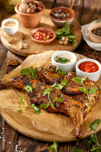 Fototapeta Naklejka Na Ścianę i Meble -  Traditional georgian dish - chicken tabaka on wooden background in rustic style. Roasted whole chicken in georgian style on wooden table. Chicken tabaka with sauces in rustic style.