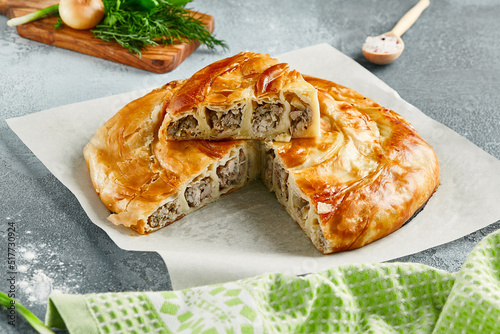 Classic turkish pie with meat on wooden board. Composition with burek pie on concrete background with textile and spices. Balkan pie with minced meat  in rustic style on gray table. photo
