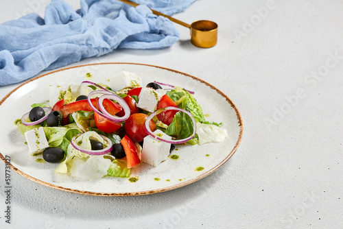 Classic greek salad with pesto sauce on ceramic plate. Vegetable salad with tomatoes, cucumber, paprika, onion and olives. Traditional grecian food. Greek salad on concrete background.