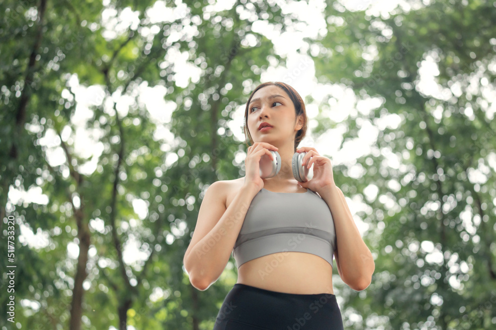 Close up asian woman adjusting wireless headphones before starting jogging and listening to music on running route surrounded by nature