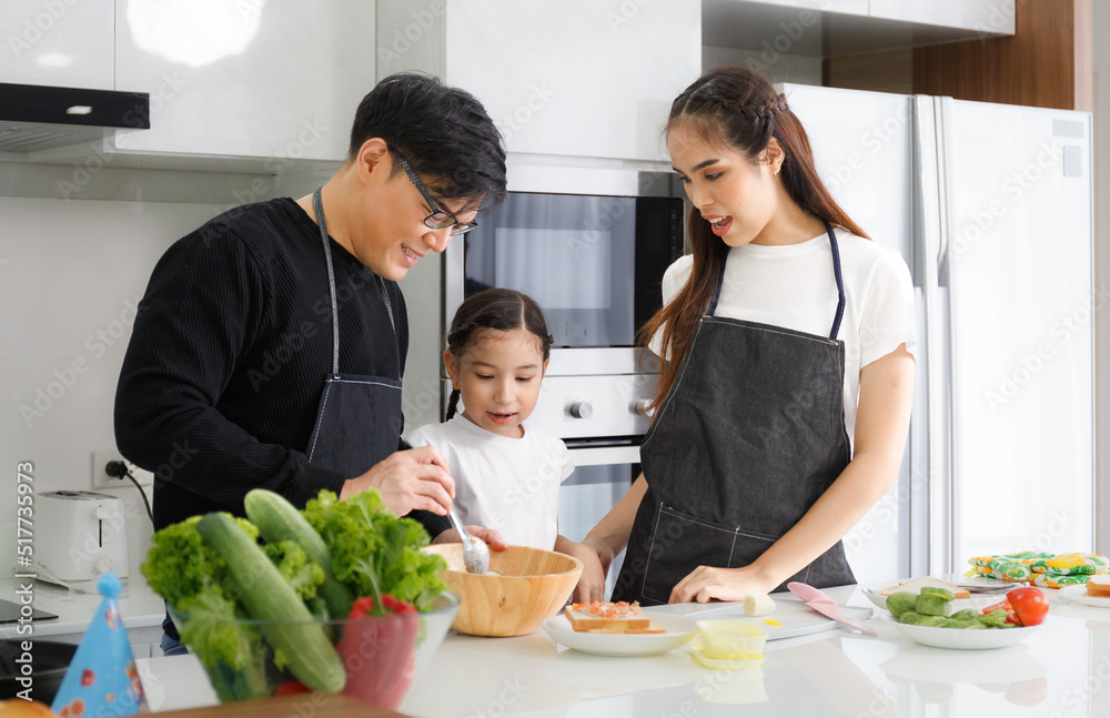 Happy family cooking together in the kitchen. Father, mother, and cute little daughter turn vegetables to make salads Happy family cooking together in the kitchen. Father, mother, and cute little daughter turn vegetables to make salads