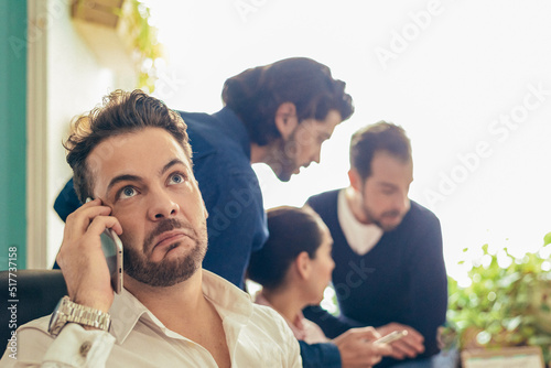 Annoyed man talking on smartphone near coworkers